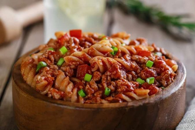 Bol en bois de fusilli à la bolognaise garnis de ciboulette verte, l'un des plats emblématiques de la cuisine italienne.