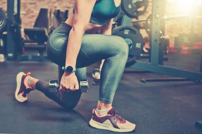 Une femme fait des fentes avec des haltères en salle de sport pour illustrer les sports idéaux pour perdre du poids