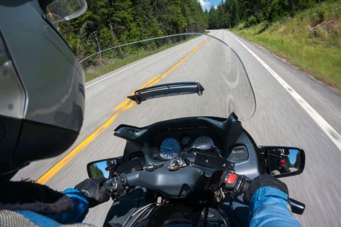 Vue subjective d'un motocycliste roulant sur une route dégagée avec un pare-brise Suzuki bien en vue.