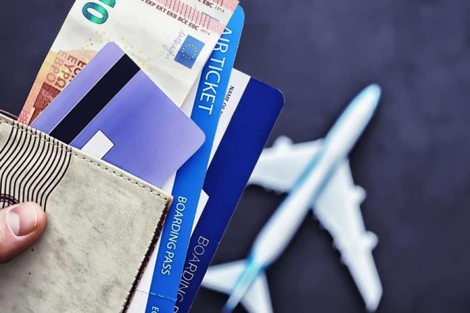 Une main tient un portefeuille contenant des billets d'avion et une carte bancaire pour réserver ses billets à la dernière minute.